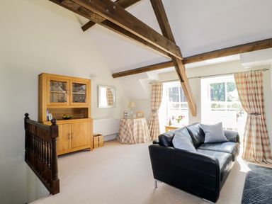 A sitting area with a black leather sofa wooden cabinet and windows with plaid curtains at Carpenters Cottage in Cockermouth