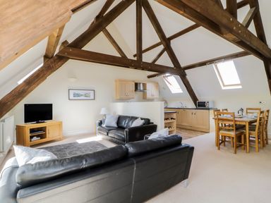 An open plan living area with black leather sofas a wooden dining table and kitchen cabinets in Carpenters Cottage in Cockermouth
