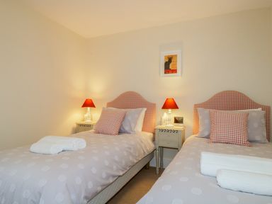 A bedroom with two single beds, bedside tables with lamps, towels on the beds and a framed picture on the wall at Carpenters Cottage in Cockermouth