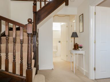 A hallway with a carpeted wooden staircase and a small white table with a lamp and flower at Carpenters Cottage in Cockermouth