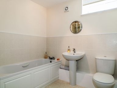 A bathroom with a bathtub sink toilet and a small round mirror at Carpenters Cottage in Cockermouth