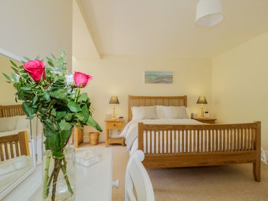 A bedroom with a wooden bed and nightstands with lamps and a vase with red roses on a dresser at Carpenters Cottage in Cockermouth