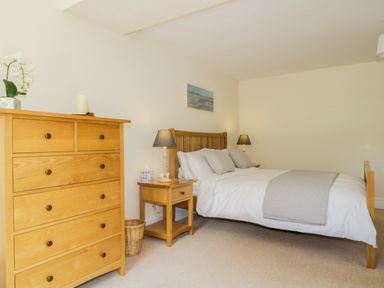 A bedroom with a wooden bed and chest of drawers and bedside table with lamps at Carpenters Cottage in Cockermouth