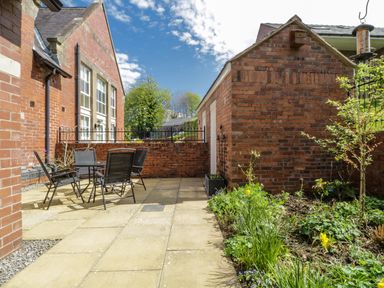 An outdoor patio area with a table and four chairs next to a brick building and a garden at Carpenters Cottage in Cockermouth