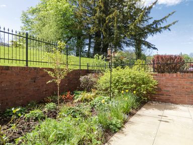 A garden with plants and flowers next to a brick wall and metal fence at Carpenters Cottage in Cockermouth