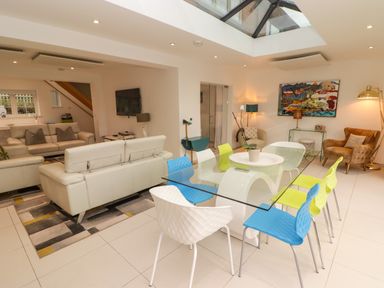 A dining area with colorful chairs and a glass table next to a living room with sofas and a television at Hiraeth in Cwmtaf near Cefn-Coed-Y-Cymmer