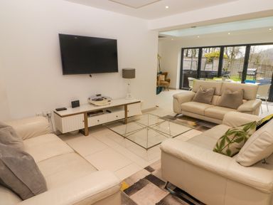 A living room with beige sofas, a glass coffee table, a wall-mounted TV, and a white console with a lamp at Hiraeth in Cwmtaf near Cefn-Coed-Y-Cymmer