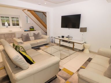 A living room with three white sofas a glass coffee table a wall-mounted television and a white console table at Hiraeth in Cwmtaf near Cefn-Coed-Y-Cymmer