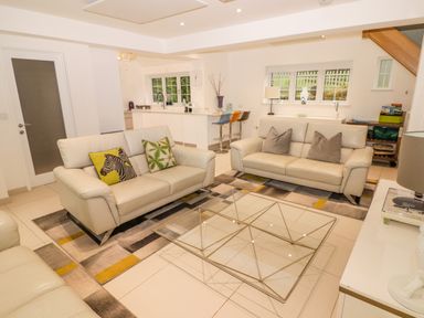 A living room with white leather sofas pillows a glass coffee table and a kitchen area with bar stools in the background at Hiraeth in Cwmtaf near Cefn-Coed-Y-Cymmer