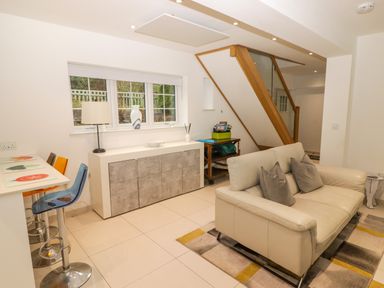A living room with a cream sofa and grey pillows next to a wooden staircase and stools at the counter at Hiraeth in Cwmtaf near Cefn-Coed-Y-Cymmer