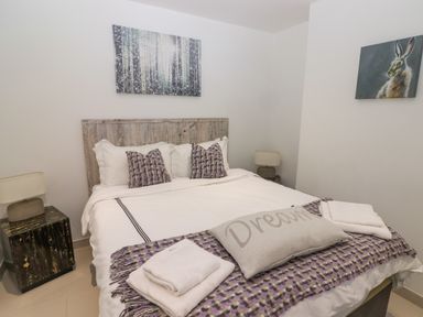 A bedroom with a double bed with white bedding and purple pillows a bedside table with a lamp and wall art of a forest and a rabbit at Hiraeth in Cwmtaf near Cefn-Coed-Y-Cymmer