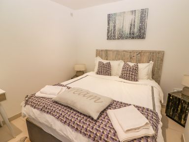 A bedroom with a bed with pillows and folded towels a side table with a lamp and a forest painting on the wall at Hiraeth in Cwmtaf near Cefn-Coed-Y-Cymmer