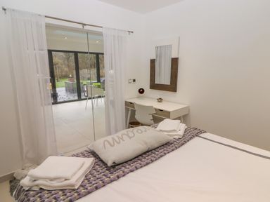 A bedroom with a bed folded towels a desk a chair a mirror and glass sliding doors leading outside at Hiraeth in Cwmtaf near Cefn-Coed-Y-Cymmer