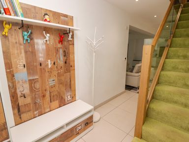 A hallway with a wooden coat rack with colorful hooks a white standing coat rack tiled floor green carpeted stairs and a view into a living room at Hiraeth in Cwmtaf near Cefn-Coed-Y-Cymmer