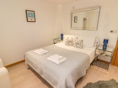 A bedroom with a bed with gray quilt and white towels on it two bedside tables with blue lamps and a large mirror on the wall at Hiraeth in Cwmtaf near Cefn-Coed-Y-Cymmer
