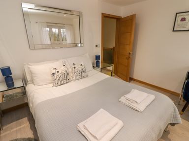 A bedroom with a bed covered with a gray quilt and white pillows two bedside tables with blue lamps a large mirror on the wall and an open wooden door at Hiraeth in Cwmtaf near Cefn-Coed-Y-Cymmer