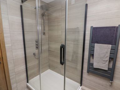 A shower enclosure with glass doors a showerhead on a tiled wall and a towel radiator with two towels at Hiraeth in Cwmtaf near Cefn-Coed-Y-Cymmer
