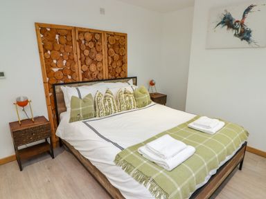 A bedroom with a bed featuring wood log panel headboard green pillows and a green blanket at Hiraeth in Cwmtaf near Cefn-Coed-Y-Cymmer