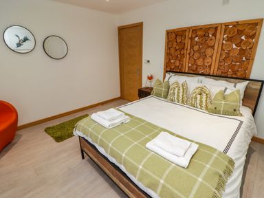 A bedroom with a bed with green pillows and a green blanket two mirrors on the wall an orange chair and a wooden door at Hiraeth in Cwmtaf near Cefn-Coed-Y-Cymmer