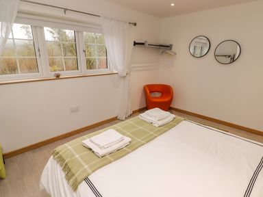 A bedroom with a bed, green checked blanket, white folded towels, two round mirrors on the wall, an orange chair and a window with white curtains at Hiraeth in Cwmtaf near Cefn-Coed-Y-Cymmer