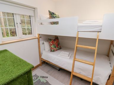A bedroom with a bunk bed a wooden ladder a window and a green grass-like chest at Hiraeth in Cwmtaf near Cefn-Coed-Y-Cymmer