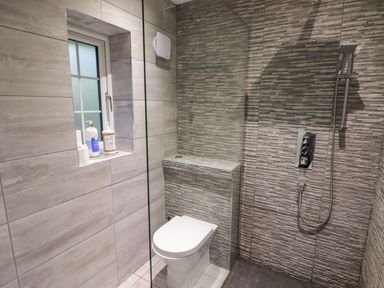 A bathroom with a toilet next to a walk-in shower and a small window with toiletry bottles on the ledge at Hiraeth in Cwmtaf near Cefn-Coed-Y-Cymmer