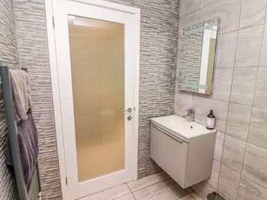 A bathroom with a wall-mounted sink and mirror next to a frosted glass door with towels hanging on a rack