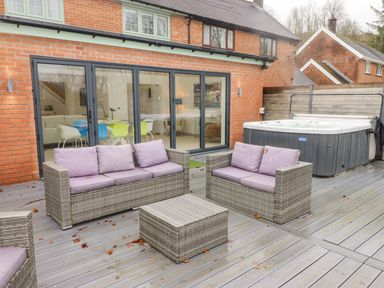 An outdoor patio with wicker furniture and a hot tub at Hiraeth in Cwmtaf near Cefn-Coed-Y-Cymmer