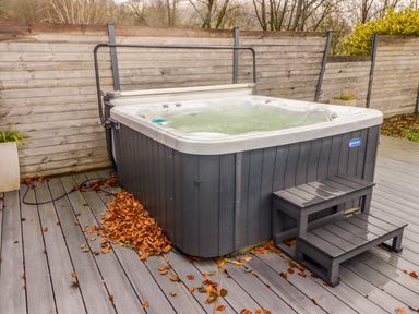 An outdoor hot tub with steps on a deck surrounded by a wooden fence at Hiraeth in Cwmtaf near Cefn-Coed-Y-Cymmer