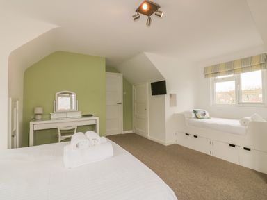 A bedroom with a large bed and rolled towels a dressing table with a mirror a single bed under a window and a small wall mounted tv at The Orchard in Crantock