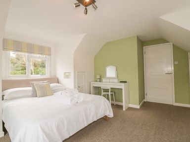 A bedroom with a bed towels and pillows near a window and dressing table with mirror and chair at The Orchard in Crantock