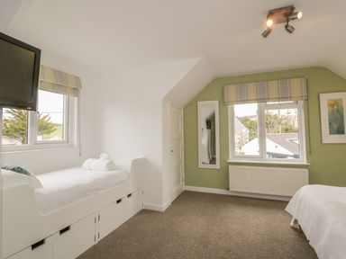 A bedroom with two single beds a wall mounted television windows and a mirror at The Orchard in Crantock