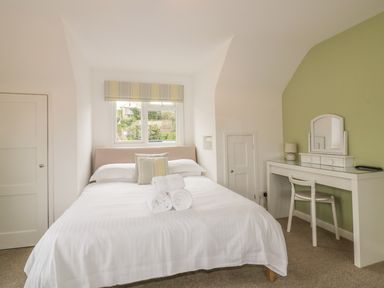 A bedroom with a bed with pillows and towels a desk with a mirror and chair and a window with striped blinds at The Orchard in Crantock