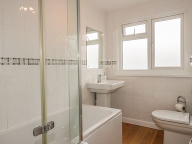 A bathroom with a bathtub shower combination a sink toilet and a window at The Orchard in Crantock