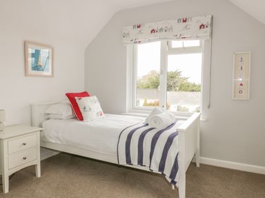 A bedroom with a single white bed white side table and window with patterned blind at The Orchard in Crantock