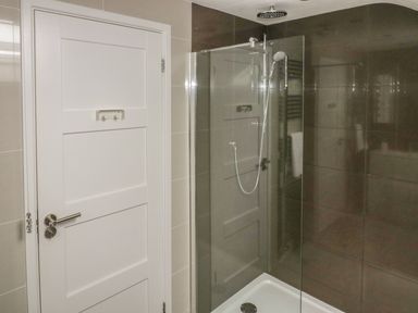 A bathroom with a walk-in shower with glass panel and a white door at The Orchard in Crantock