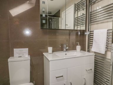 A bathroom with a white sink cabinet a mirror towel rack with a white towel and a toilet at The Orchard in Crantock