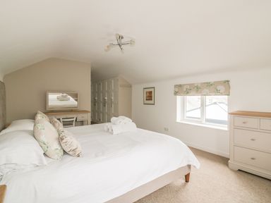 A bedroom with a double bed towels on bed wall mirror desk chair window with floral valance chest of drawers at The Orchard in Crantock