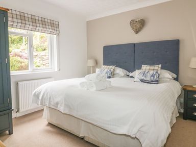 A bedroom with a double bed with blue headboard bedside tables and a window at The Orchard in Crantock