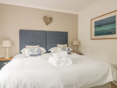 A bedroom with a bed with blue headboards white bedding rolled towels bedside tables with lamps and wall art at The Orchard in Crantock