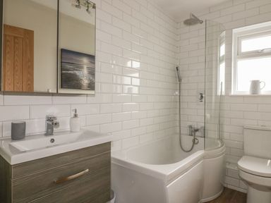 A bathroom with a bathtub shower combination, a sink with a cabinet, a toilet and a window at The Orchard in Crantock