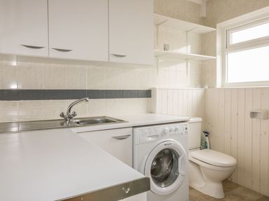 A laundry room with a washing machine sink toilet and shelves at The Orchard in Crantock