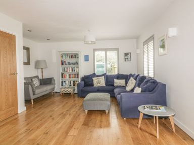 A living room with a blue sectional sofa a gray armchair a bookshelf a wooden floor and a round side table at The Orchard in Crantock
