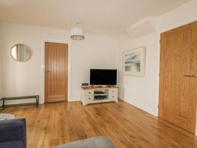 A living room with wooden floors a television on a stand and two wooden doors at The Orchard in Crantock