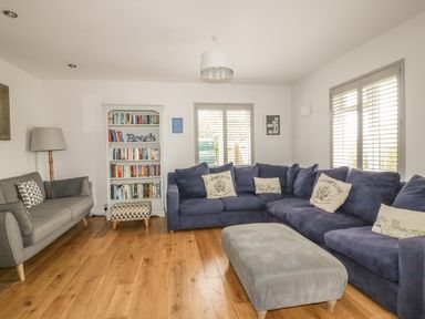 A living room with a grey sofa a blue corner sofa a bookshelf and a grey ottoman at The Orchard in Crantock