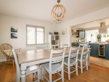 A dining area with a long table and chairs next to a kitchen with blue cabinets at The Orchard in Crantock