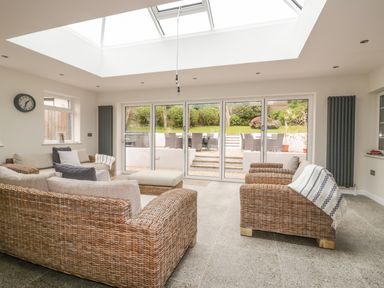 A living room with wicker furniture and sliding glass doors leading to a garden at The Orchard in Crantock