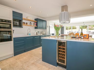 A kitchen with blue cabinets a kitchen island with wine cooler and flowers on the island at The Orchard in Crantock