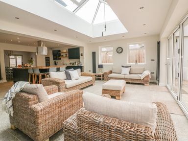 A sitting area with wicker sofas and cushions under a skylight near a kitchen and dining area at The Orchard in Crantock