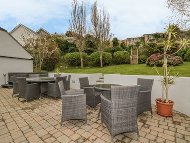 An outdoor patio area with gray wicker tables and chairs and a potted plant overlooking a garden with stairs leading up at The Orchard in Crantock